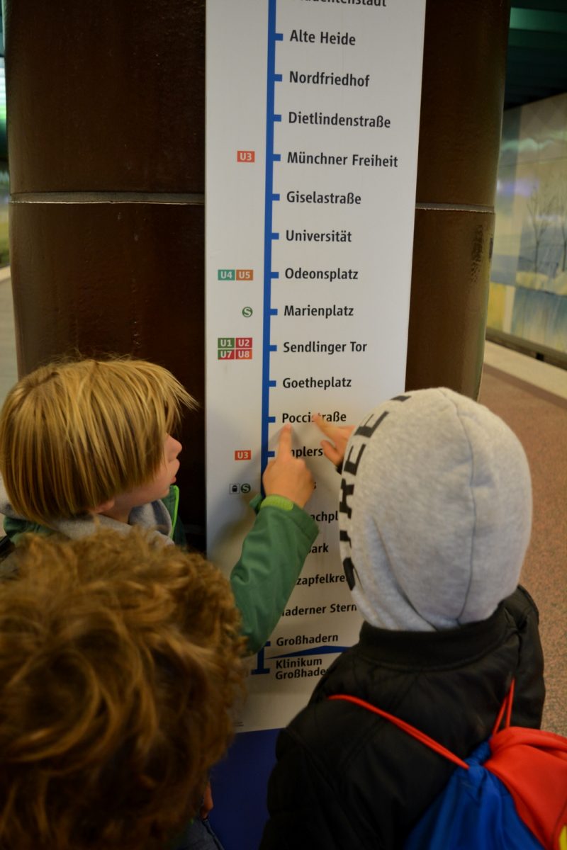 Junge Schüler*innen schauen sich den Fahrplan an und fahren diesen mit dem Finger nach.